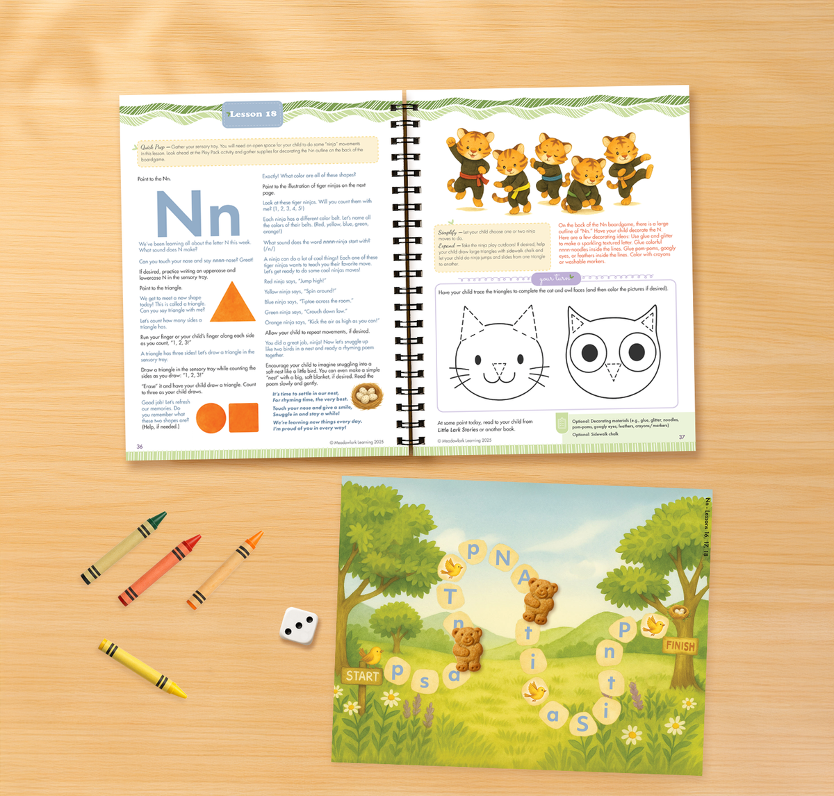 Open educational book on a wooden surface with crayons and a game card.