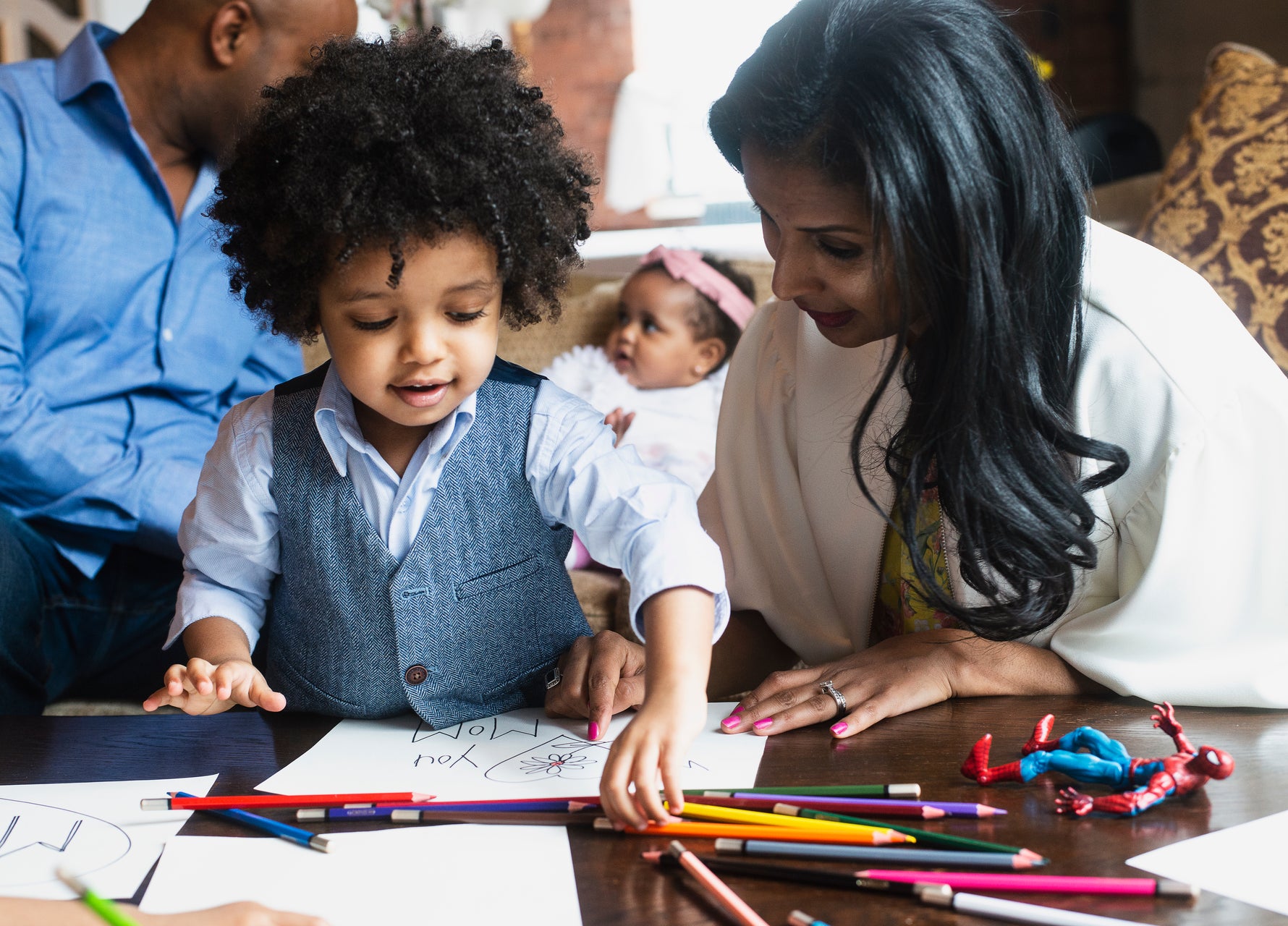 woman and child at table drawing with colored pencils and spiderman toy laying on table